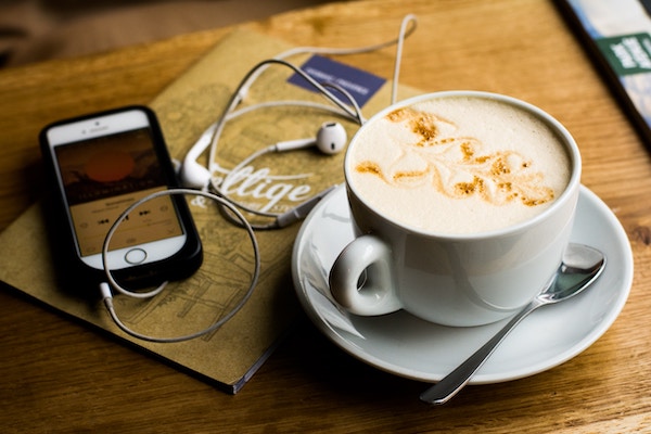 Ein iPhone mit Apple-Kopfhörern liegt auf einem Tisch. Daneben eine Tasse mit Kaffee.
